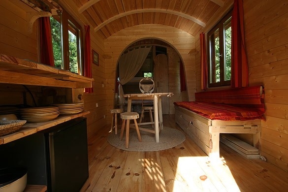 Photo du séjour de la roulotte avec le plan de travail, la banquette pouvant faire lit 2 personnes ainsio que les lits superposés dans le fond de la roulotte. 